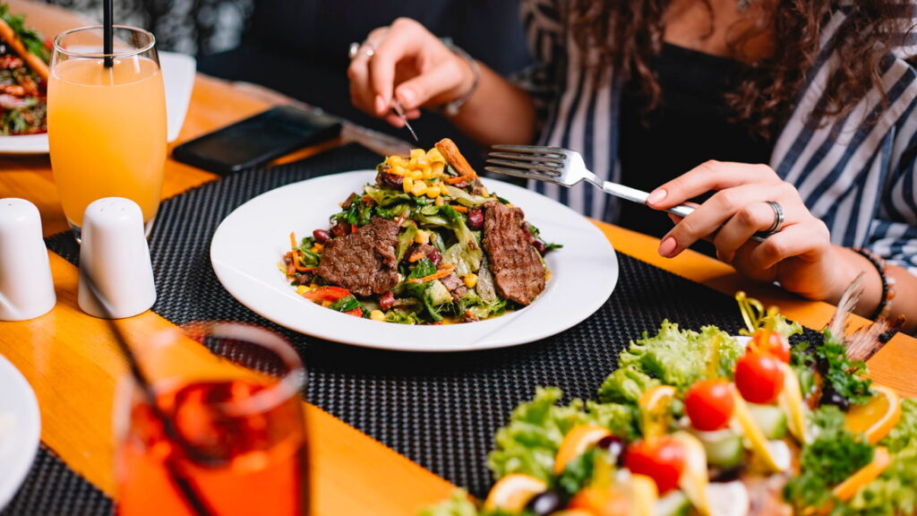 Woman enjoying healthy steak salad with refreshing drinks