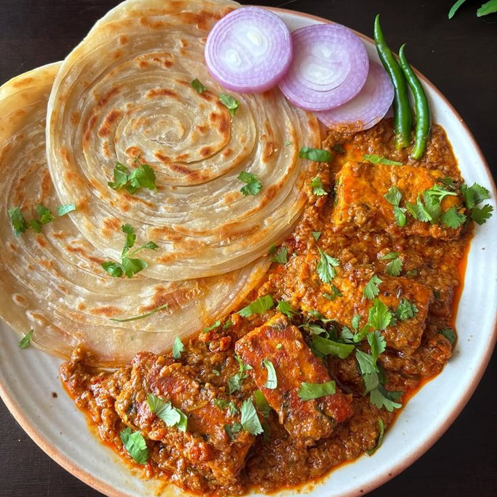 Spicy chicken curry served with flaky paratha and onions